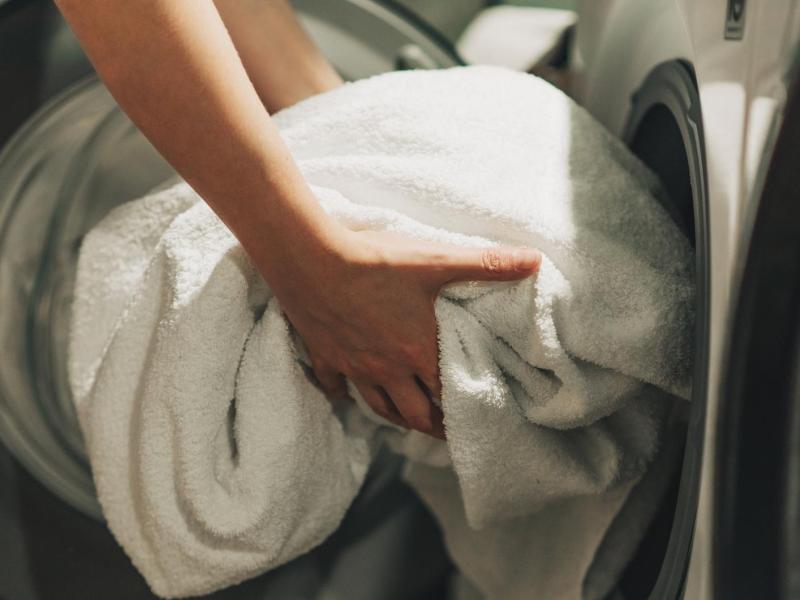 Frau legt ein großes Badetuch in die Waschmaschine.