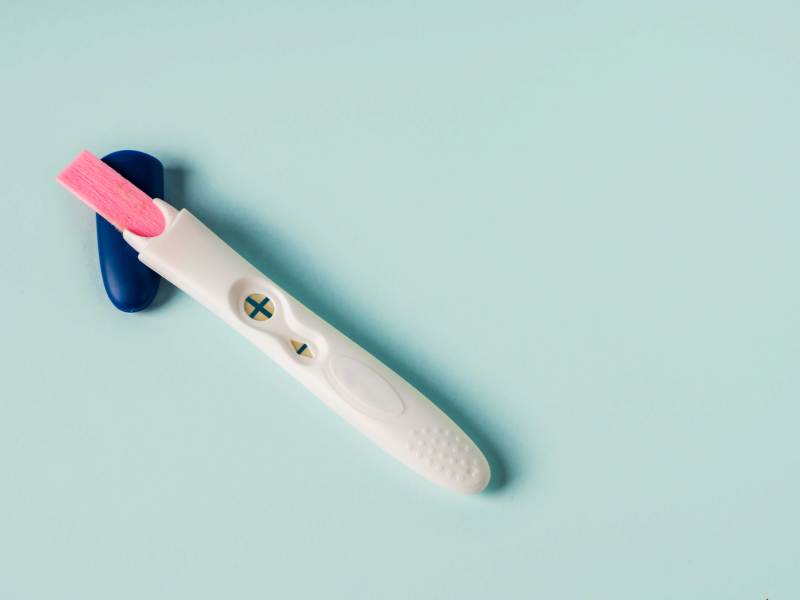 Positiver Schwangerschaftstest vor türkisem Hintergrund.