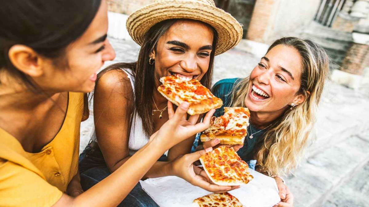 Drei Freundinnen lachen und essen Pizza.