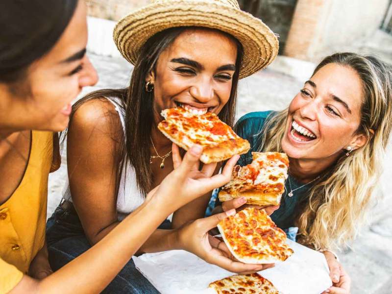 Drei Freundinnen lachen und essen Pizza.
