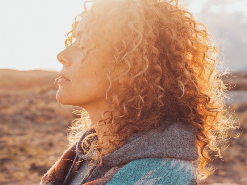 Frau in der Natur mit Locken, die genussvoll in die Sonne blickt