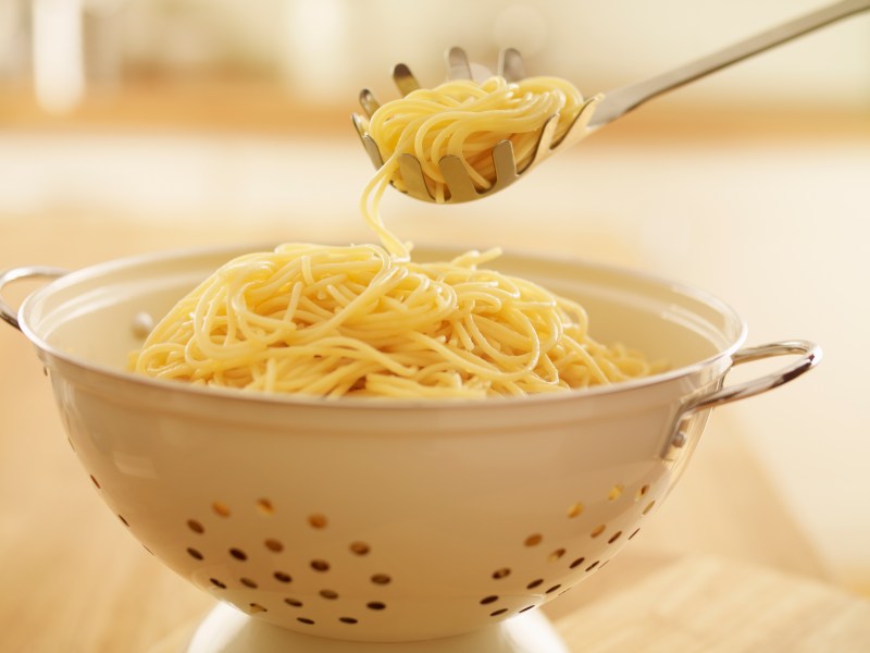 Spaghetti in Sieb werden mit Spaghetti-Löffel portioniert