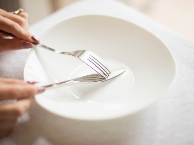 Eine Person schneidet mit einem Messer auf einem Teller