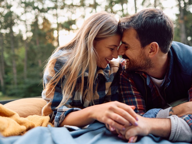 Mann und Frau auf einer Picknick-Decke, die ihren Nasen aneinander halten und lächeln
