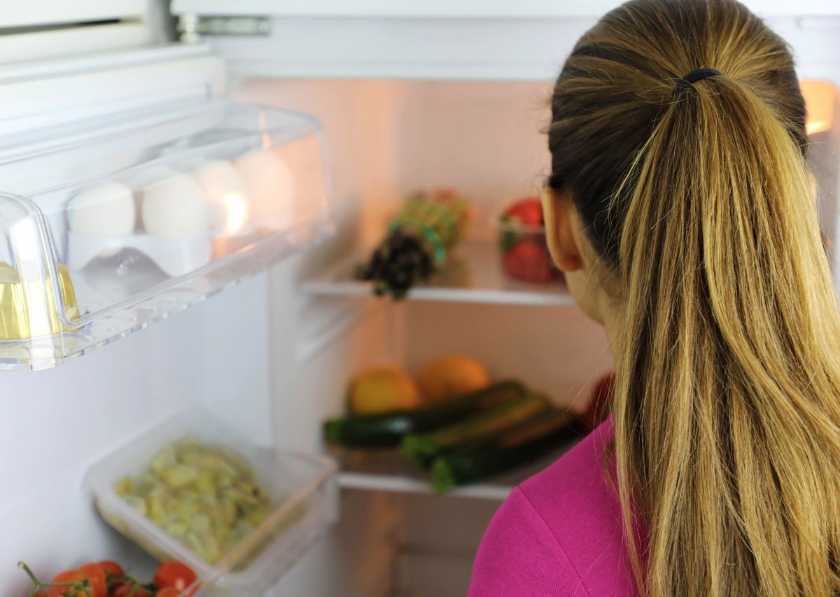 Eine Frau schaut in den offenen Kühlschrank.