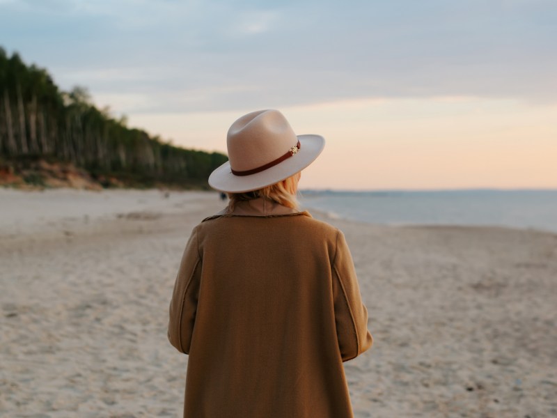 Frau mit Hut am Strand, die in den Sonnenuntergang läuft