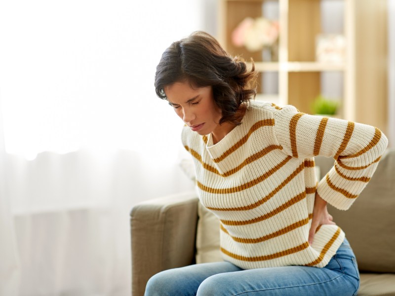 Eine Frau mit Ischiasschmerzen hält sich den Rücken.