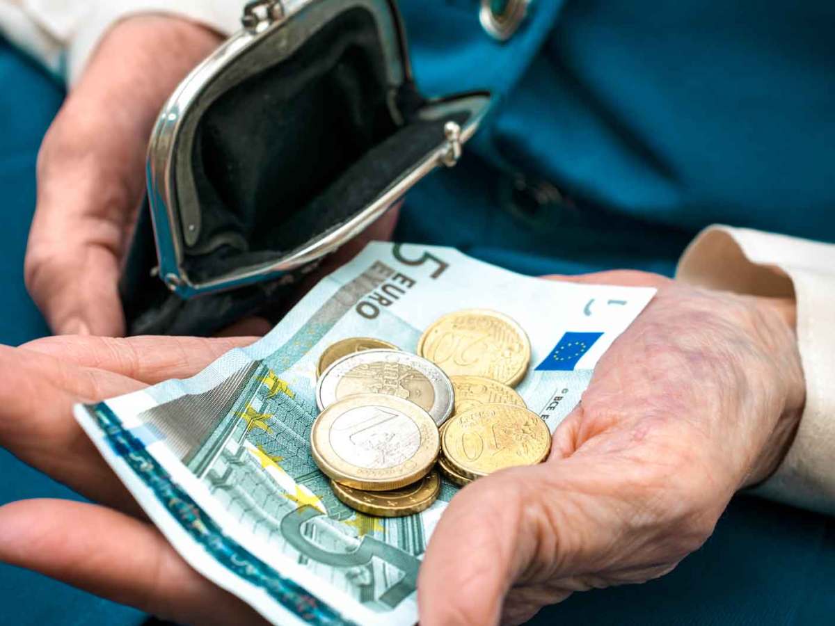 Ältere Frau hat Geld aus ihrer Geldbörse genommen und hält Scheine und Münzgeld in der Hand.