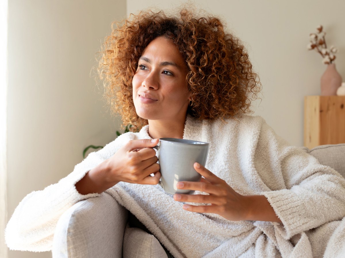 Frau sitzt auf dem Sofa und hält eine Tasse Kaffee in der Hand