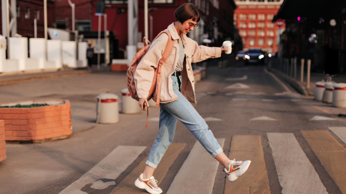 Junge Frau in Jeans läuft über Straße.