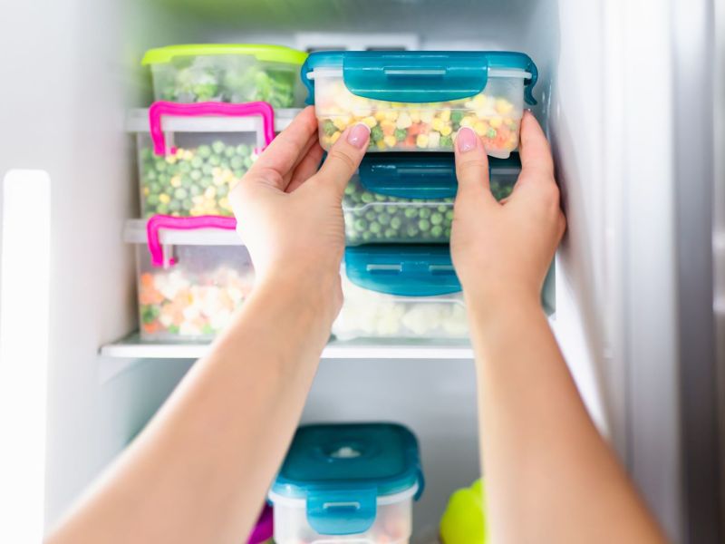 Frauenhände legen Plastikdosen mit Lebensmittel in den Gefrierschrank