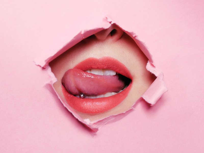 Mund mit Zunge vor einem Loch in einer pinken Wand