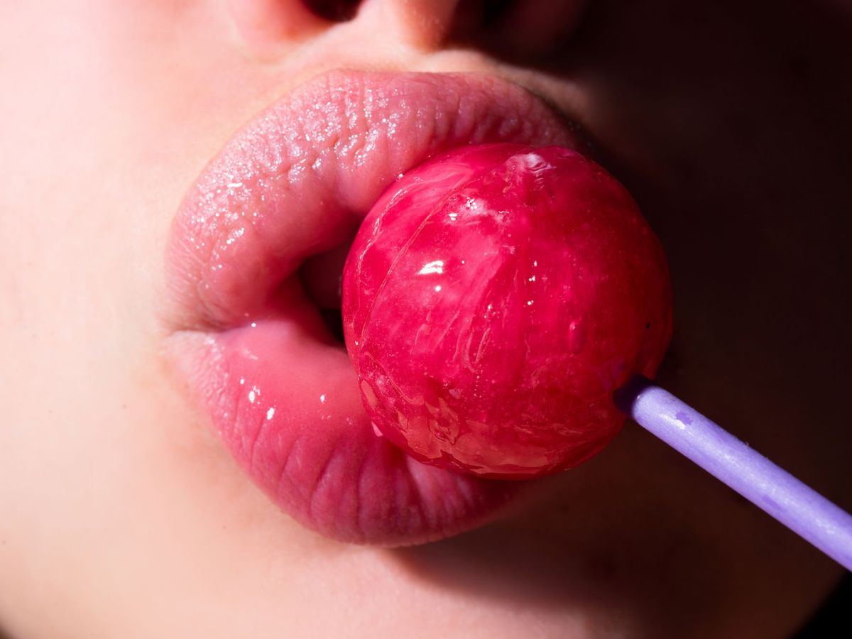 Lippen umschließen einen pinken Lolli als Symbolbild für einen Blowjob