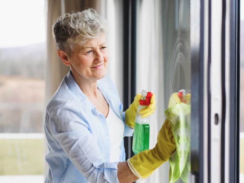 ältere Frau putzt Fenster
