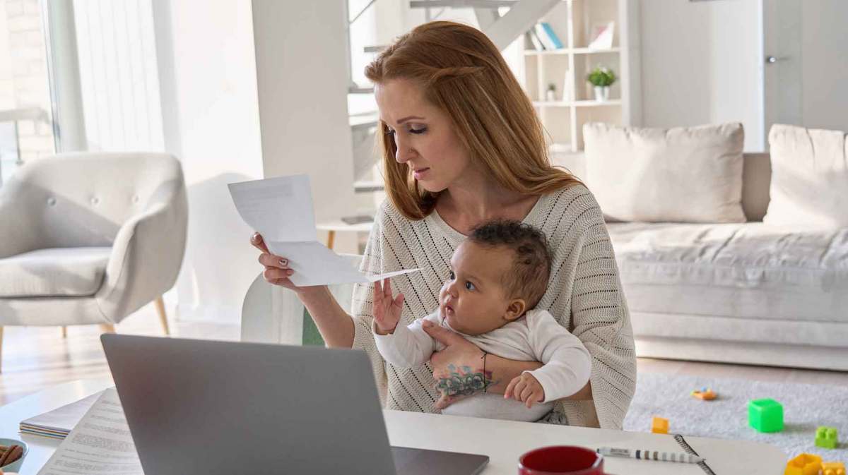 Frau mit einem Kleinkind sitzt am Tisch und sieht sich ein Dokument an.