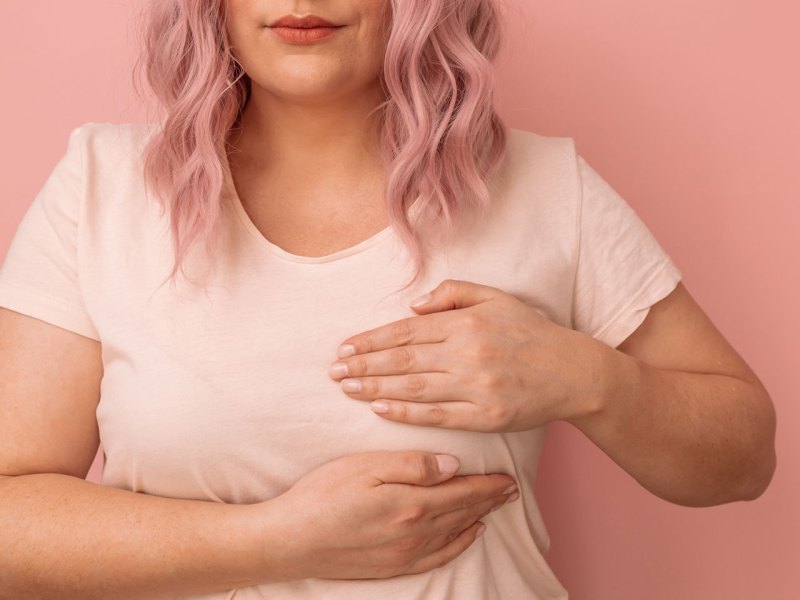 Frau tastet ihre Brust ab vor einem rosa Hintergrund
