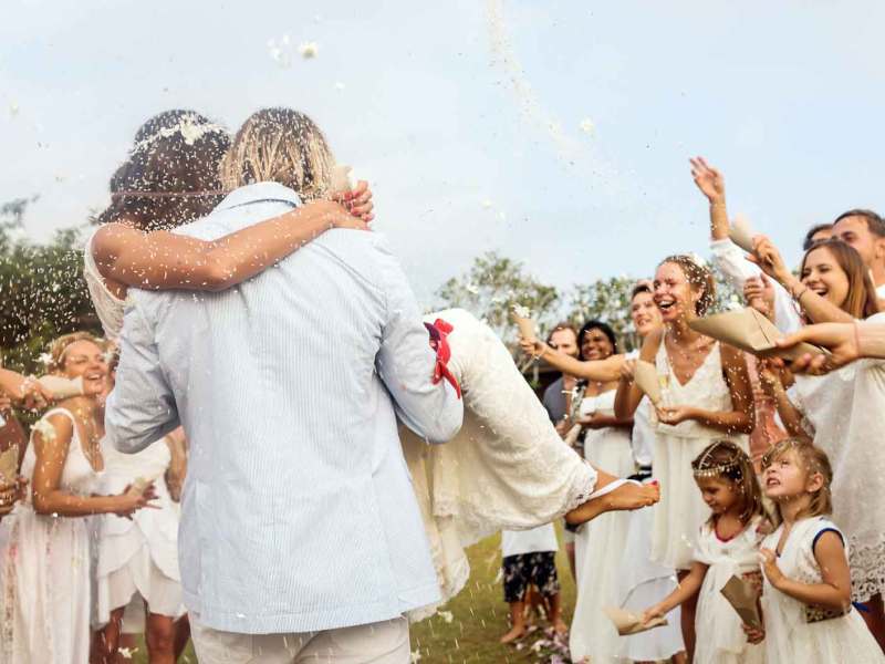 Bräutigam trägt seine Braut auf Händen durch die feiernde Menge.