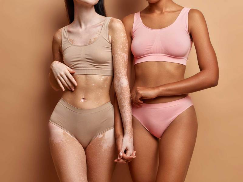 Jeder Körper ist schön. Zwei Frauen unterschiedlicher Hautfarbe in Dessous posieren vor einem beigen Hintergrund.