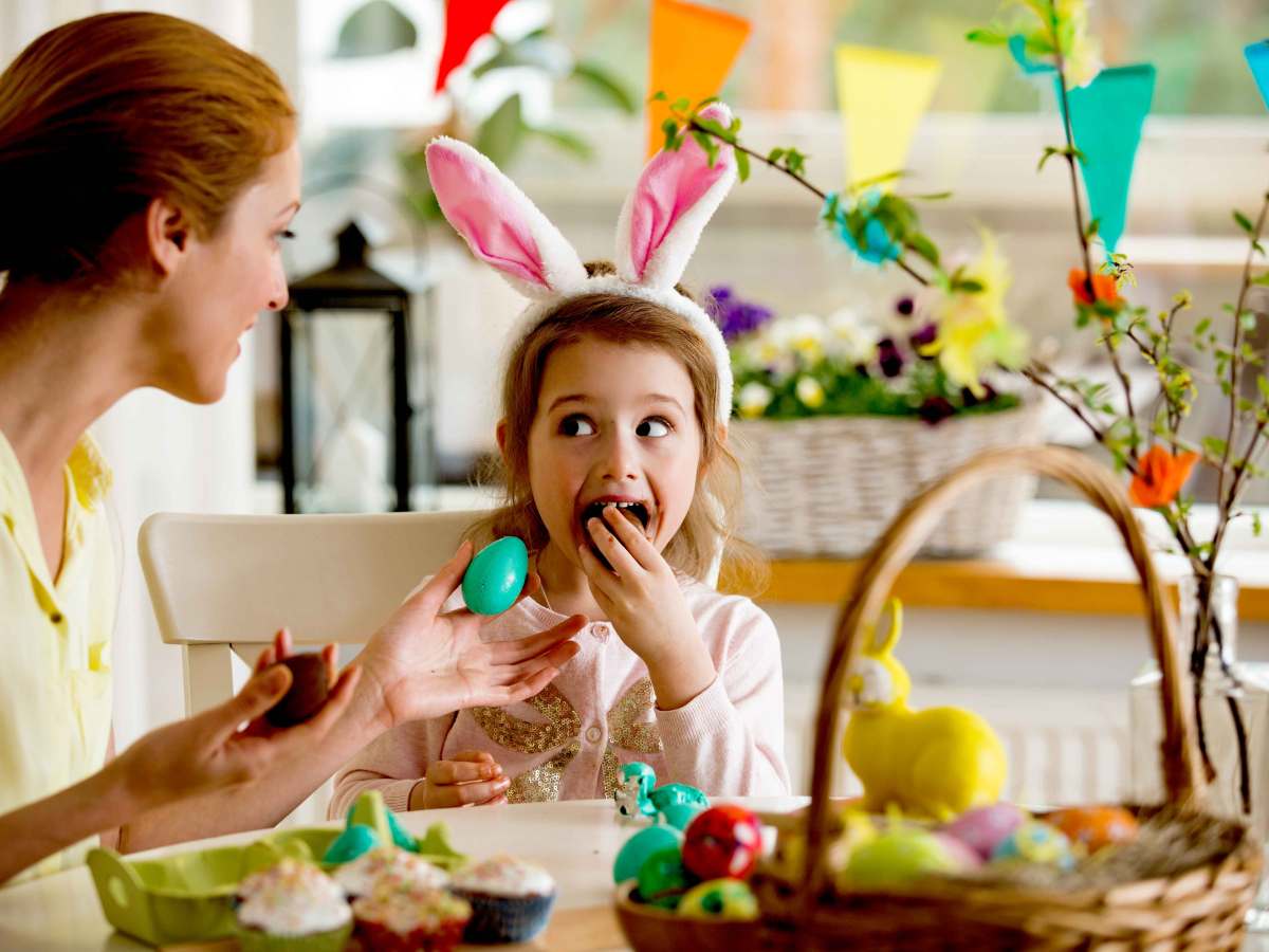 Mädchen und Mutter sitzen zu Ostern am Küchentisch und genießen Schokoladeneier.