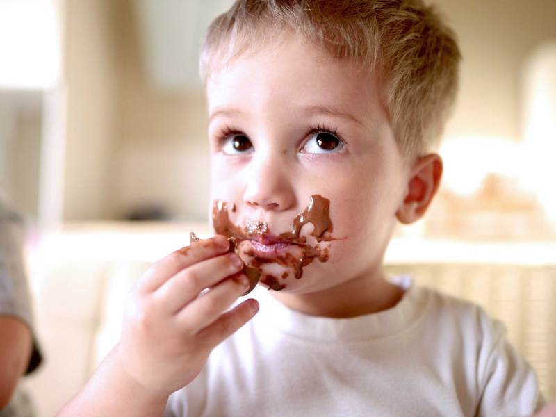 Kleiner Junge isst Schokolade und hat bereits einen Schoko-verschmierten Mund.