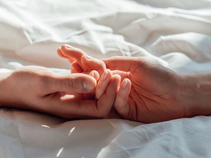 Zwei Hände auf einem weißen Bettlaken, die sich aneinander halten