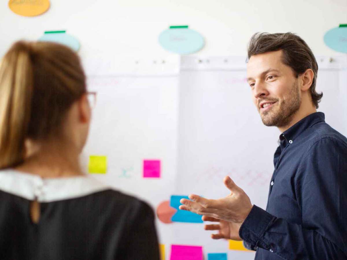 Mann erklärt einer Frau etwas vor einem Flipchart.