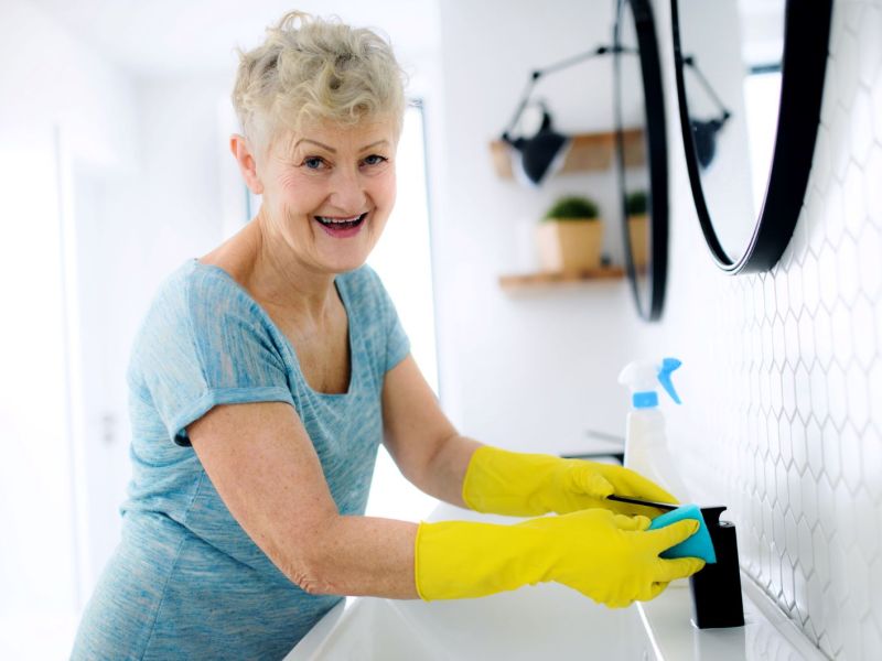 Eine ältere Frau putzt das Badezimmer mit Gummihandschuhen an