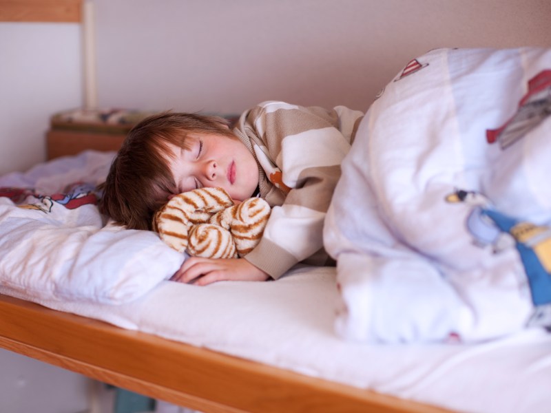 Junge, ca. 7 Jahre, liegt im Bett und macht Mittagsschlaf.