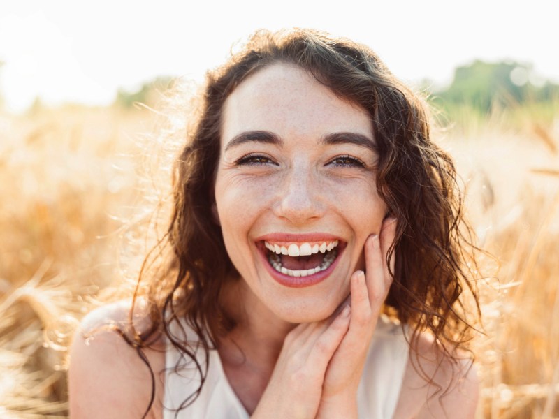 Frau in einem Feld von Sonne umgeben, die lachend in die Kamera schaut