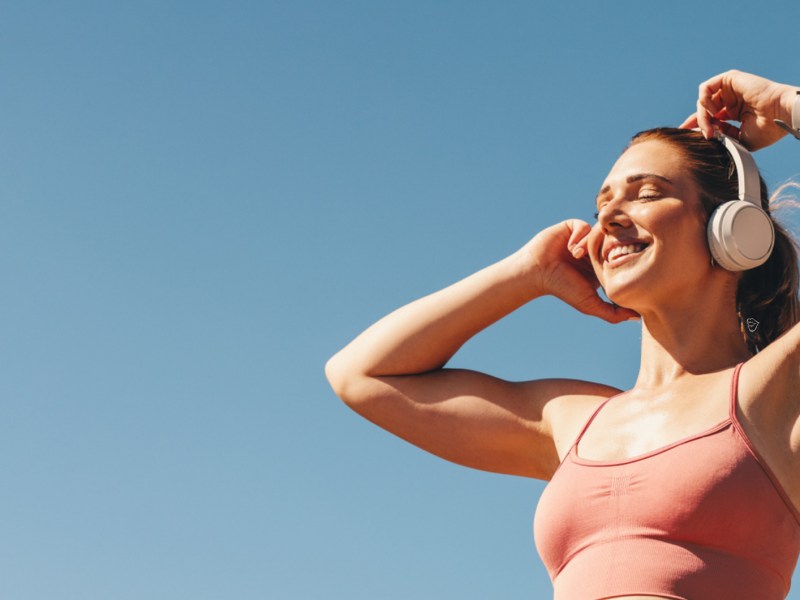 Frau in der Sonne in Sportklamotten, die lächelt und sich Kopfhörer aufzieht