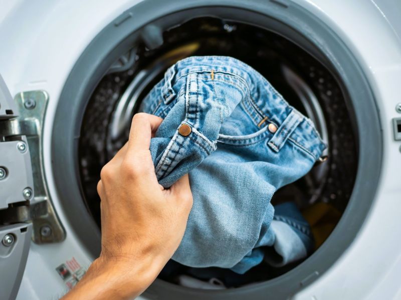 Hand steckt Jeans in Waschmaschine