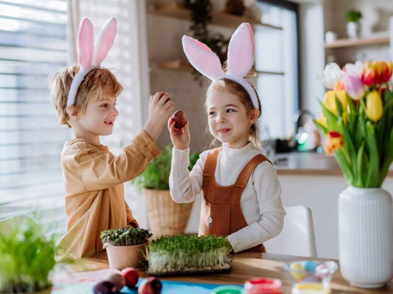 Kleine Kinder mit Hasenohren feiern Ostern und spielen ein Osterspiel mit Eiern.
