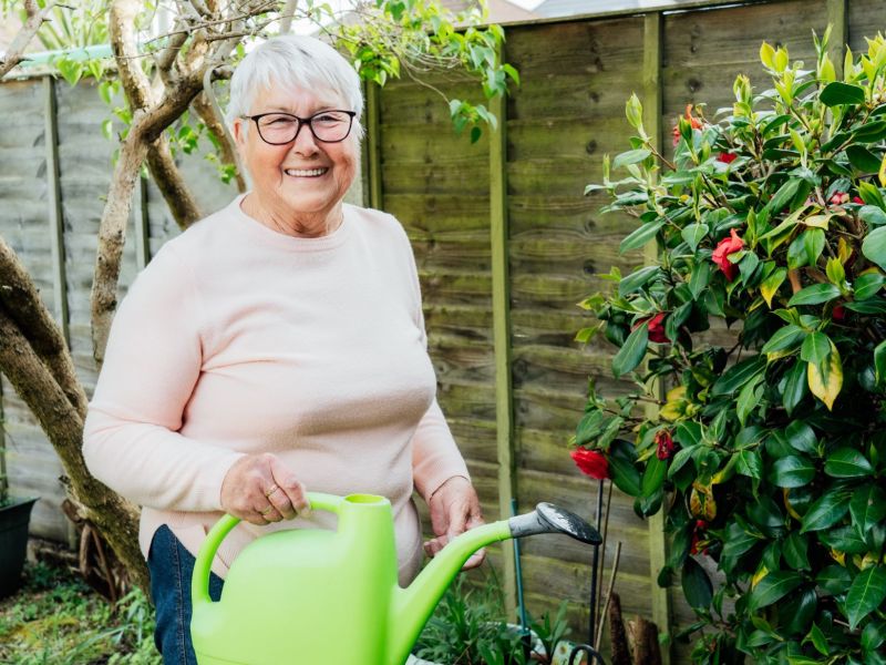 Ältere Frau im Garten mit grüner Gießkanne