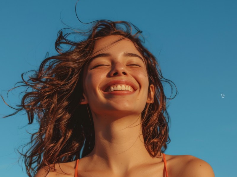 Frau mit blauem Himmel im Hintergrund, die glücklich lächelt