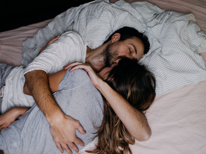 Paar liegt Arm in Arm im Bett und schläft