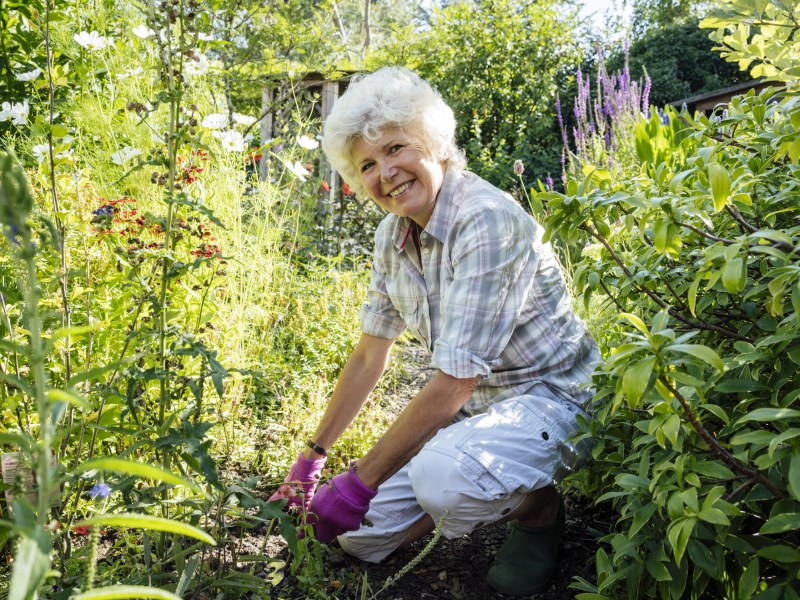 Omas Hausmittel gegen Unkraut: Ältere Dame kniet in Garten