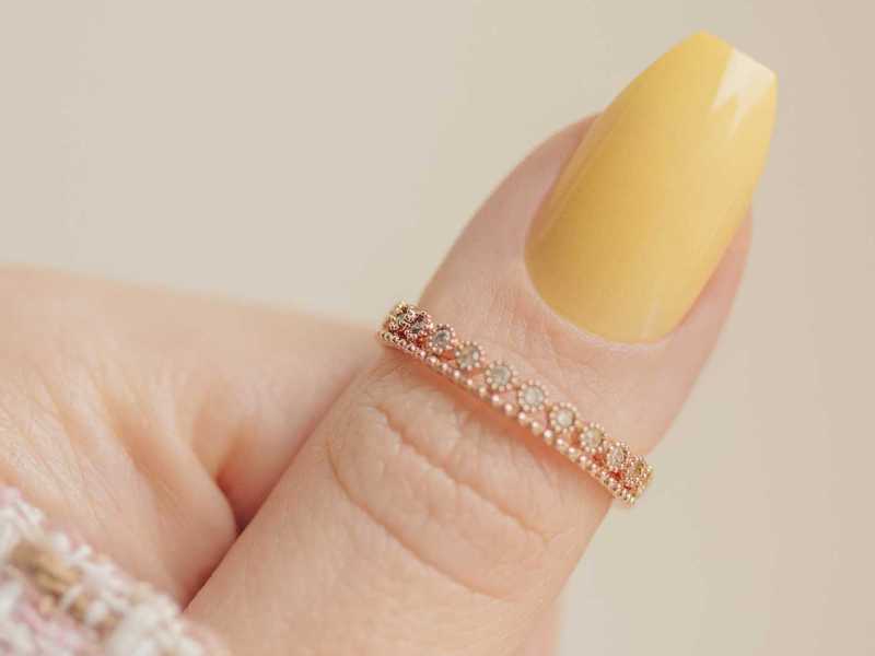 Daumen mit einem gelb lackierten Fingernägel und einem goldenen Ring
