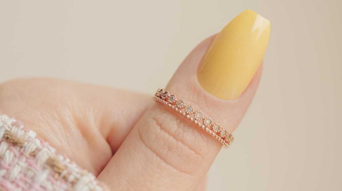 Daumen mit einem gelb lackierten Fingernägel und einem goldenen Ring