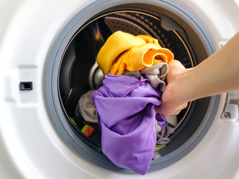 Hand legt Schlafanzug zum Waschen in Waschmaschine