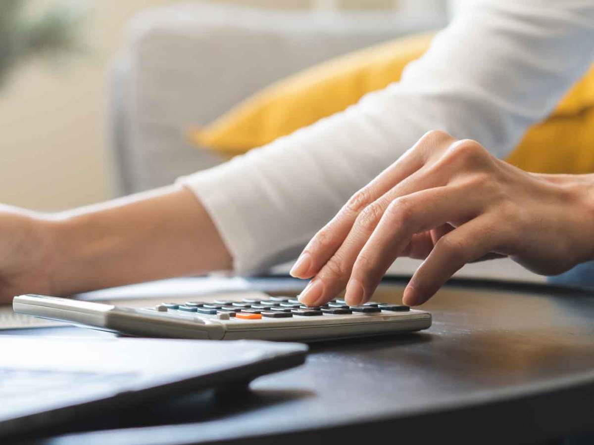 Frau sitzt zuhause an einem Tisch vor einem Laptop und rechnet mit einem Taschenrechner ihre Steuern aus.