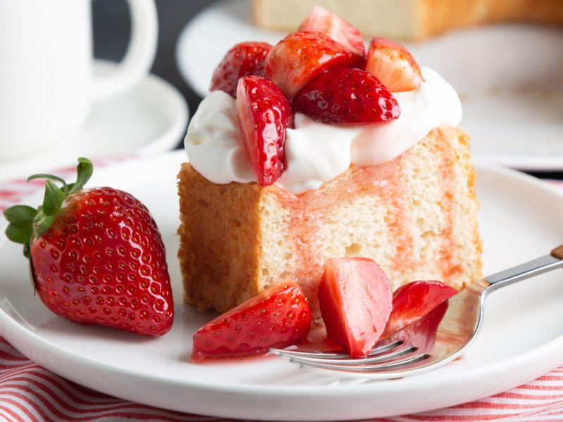 Angel Food Cake mit Erdbeeren und Sahne auf weißem Kuchenteller.