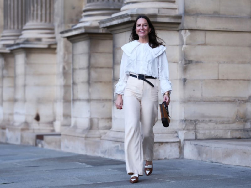 Frau in weißer Bluse und beiger Hose läuft durch Paris.