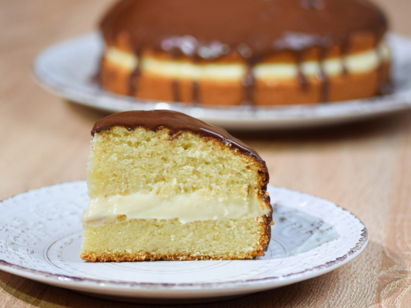 Boston Cream Pie auf einem hellen Kuchenteller.