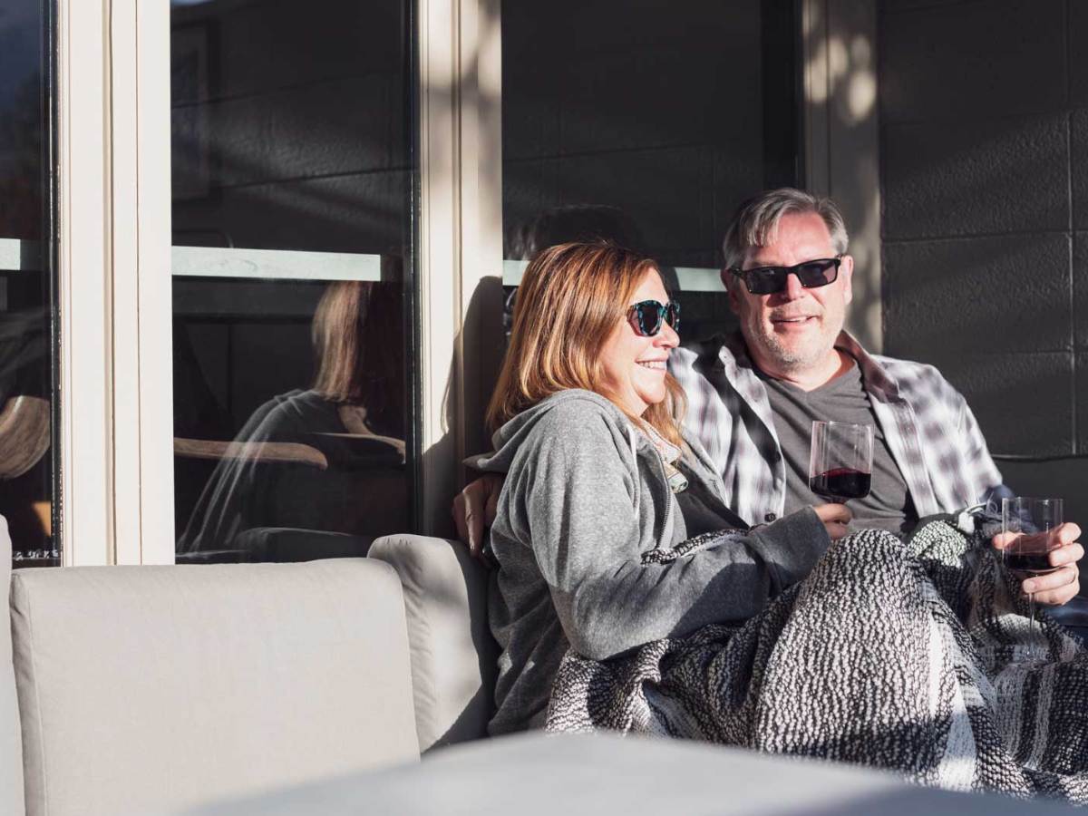Paar mittleren Alters sitzt auf der Terrasse in der Sonne und genießt ein Glas Rotwein.