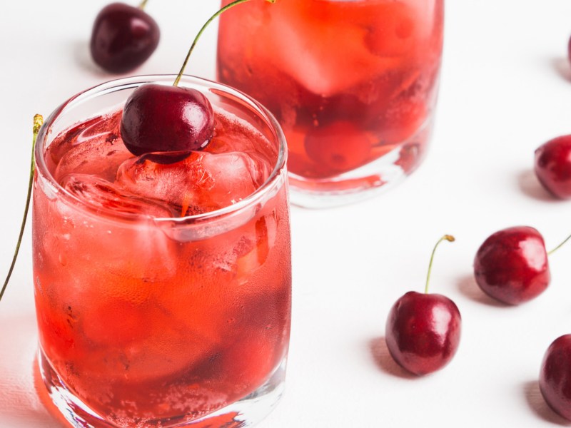 Roter Cocktail mit Eiswürfeln und Kirschen.