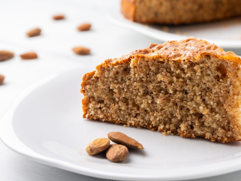 Ein Stück dunkler Mandelkuchen auf einem weißen Teller.