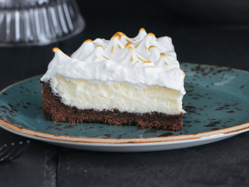 Torte mit dunklem Boden, Puddingschicht und Sahne auf einem blauen Teller.