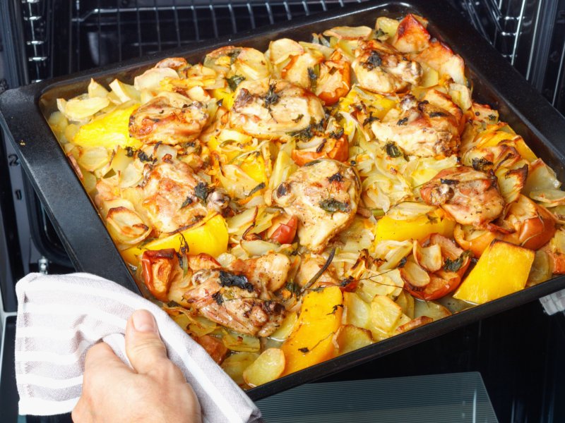 Person holt Backblech mit Hähnchen, Paprika und Kartoffeln aus Ofen.