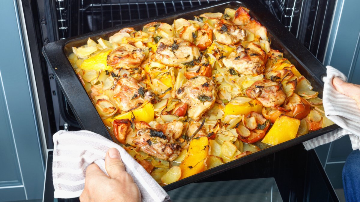 Person holt Backblech mit Hähnchen, Paprika und Kartoffeln aus Ofen.