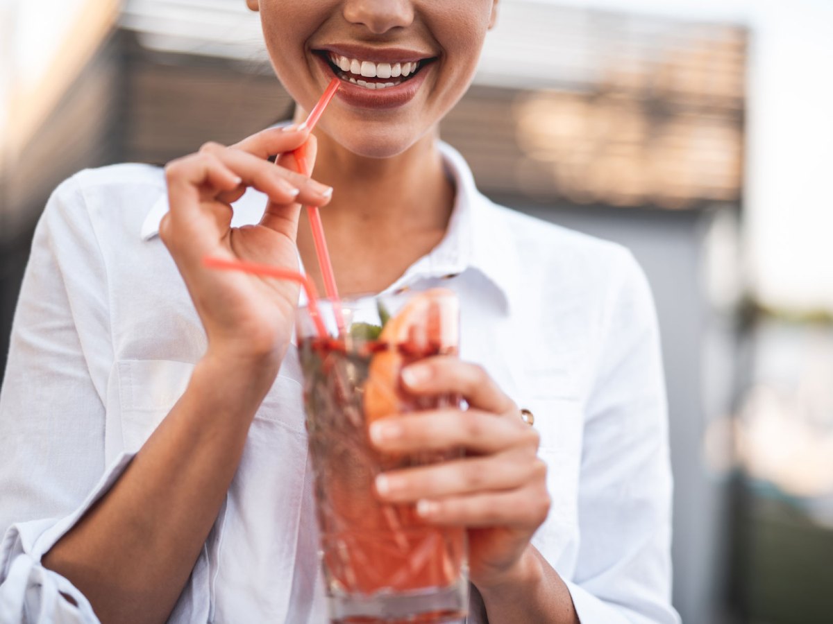Frau hält Cocktail in der Hand und lächelt